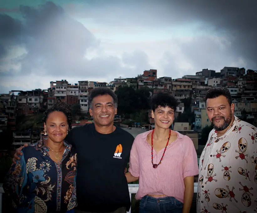 A diretoria do Grupo Nós do Morro reunida em um mirante do Vidigal, com as casas do morro ao fundo ao entardecer