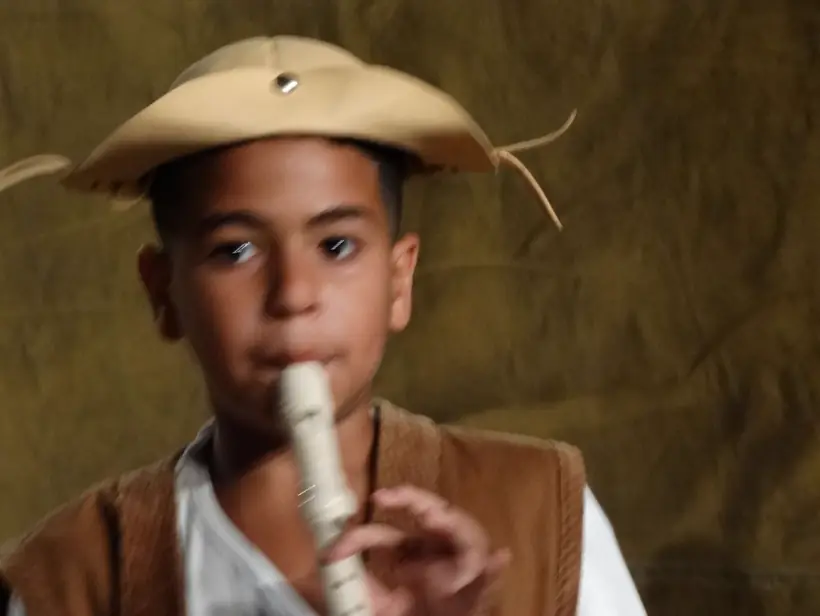 Menino de chapéu de palha soprando um apito, em primeiro plano